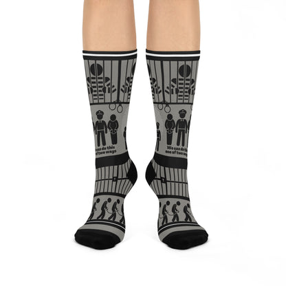 A pair of black and white crew socks with a geometric pattern, featuring designs that include cubes and what appears to be a representation of a police station or jail.