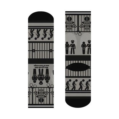 A pair of black and white crew socks with a geometric pattern, featuring designs that include cubes and what appears to be a representation of a police station or jail.