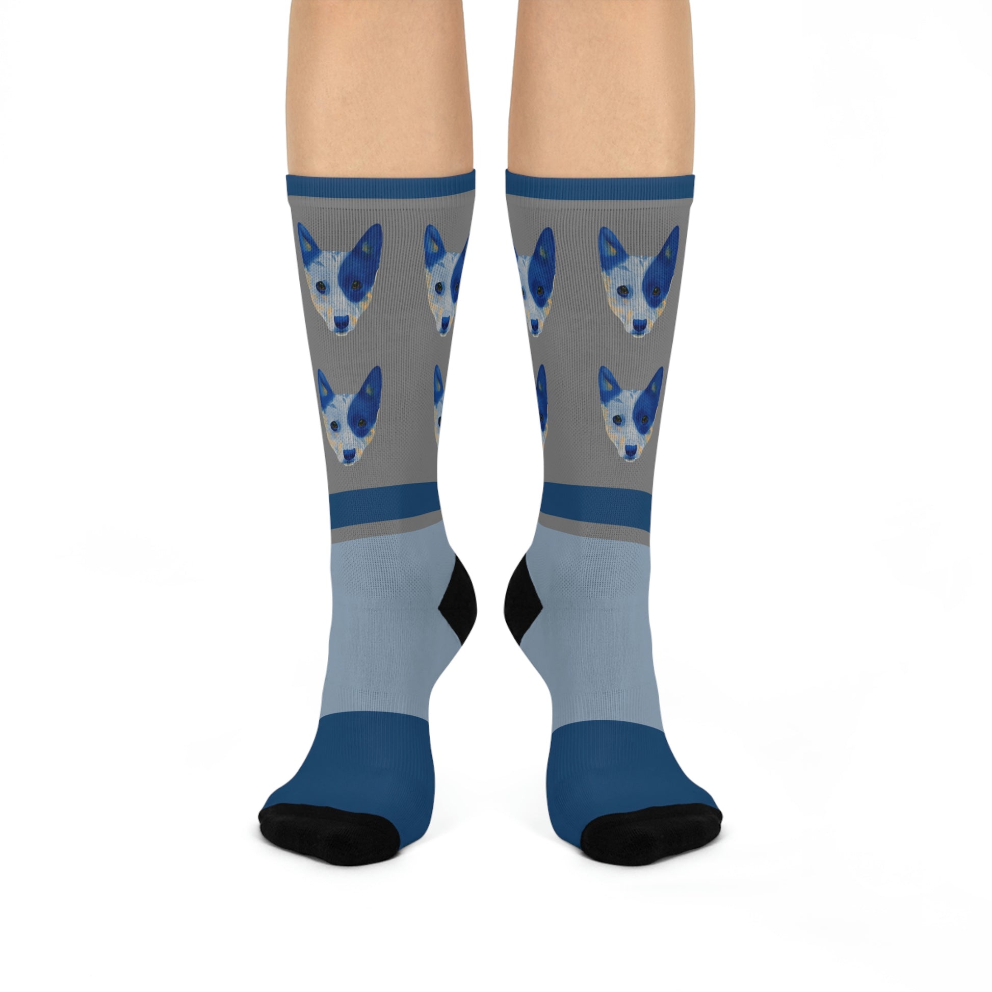 A pair of blue and gray mid-calf socks with a design of two blue healer dogs and a part of a human foot visible.