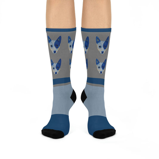 A pair of blue and gray mid-calf socks with a design of two blue healer dogs and a part of a human foot visible.